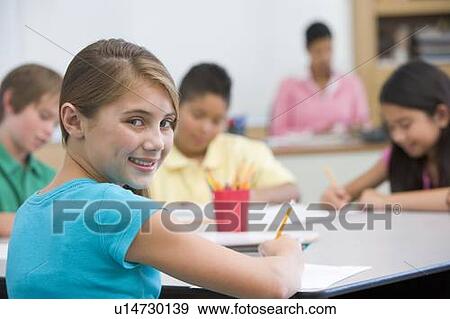 Stock Photo - Students in class taking notes with teacher in background (selective focus). Fotosearch