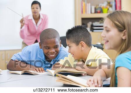 Stock Image - Students in class talking with teacher in background (selective focus). Fotosearch