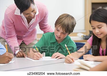 Picture - Students in class writing with teacher helping. Fotosearch
