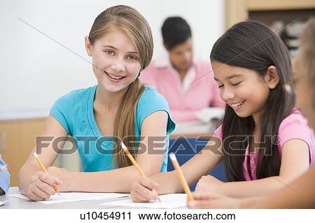 Stock Image - Students in class writing with teacher in background (selective focus). Fotosearch