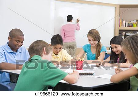 Stock Photo - Students in class writing with teacher at front board. Fotosearch