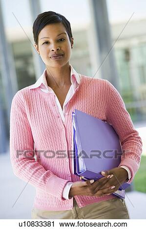 Stock Image - Teacher standing outside school holding binders (selective focus). Fotosearch