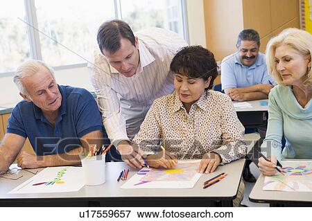 Stock Photo - Adult students in class drawing pictures with teacher helping (selective focus). Fotosearch