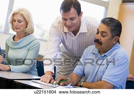 Adult students in class with teacher helping View Large Photo Image Picture - Adult students in class with teacher helping. Fotosearch