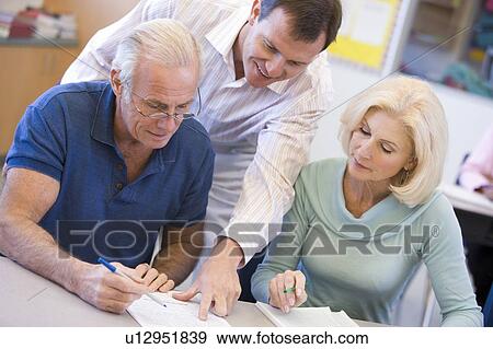 Stock Photo - Adult students in class with teacher helping. Fotosearch