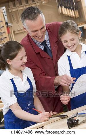 Stock Photograph - Female students reviewing woodworking plans with teacher. Fotosearch
