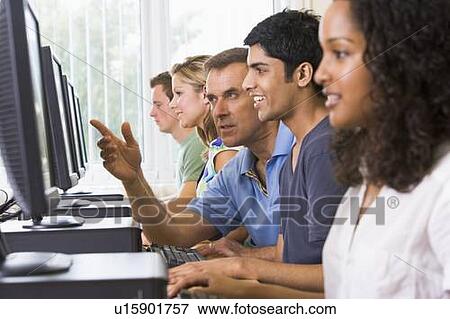 Stock Photo - Four students sitting at computer terminals with teacher helping one of them (depth of field/high key). Fotosearch
