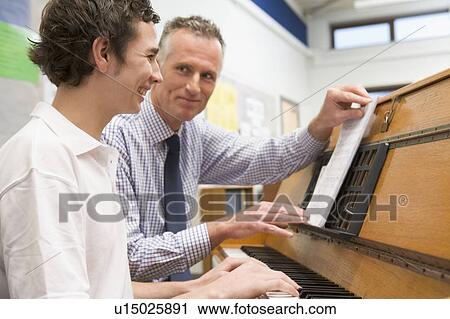 Stock Image - Male student learning piano with teacher in classroom. Fotosearch