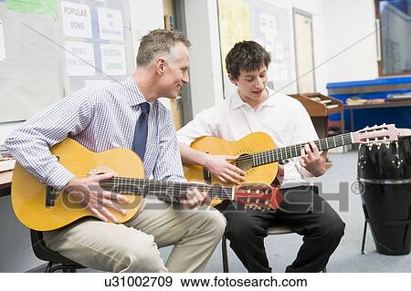 Male student receiving guitar lesson from teacher in classroom View Large Photo Image Stock Photo - Male student receiving guitar lesson from teacher in classroom. Fotosearch