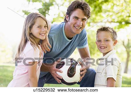 Stock Image - Man and two young children outdoors holding volleyball and smiling. Fotosearch