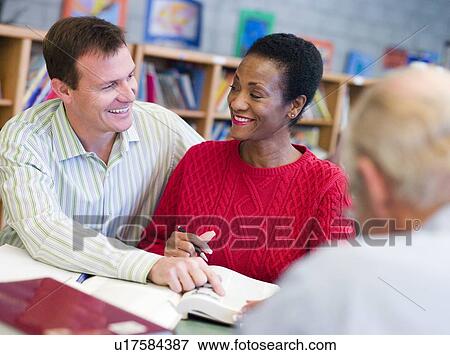 Stock Photo - Man and woman sitting in library near another man with a book and notepad (selective focus). Fotosearch