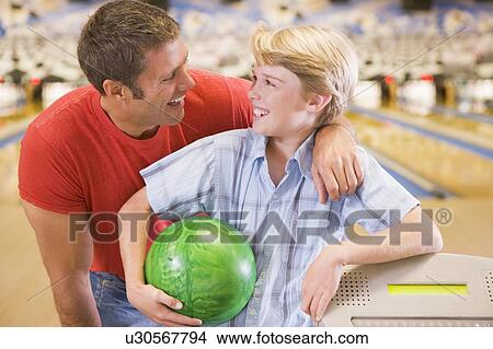 Picture - Man and young boy in bowling alley holding ball and smiling. Fotosearch