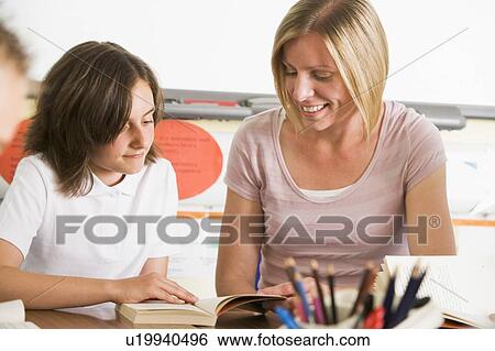 Stock Photograph - Student in class reading book with teacher. Fotosearch