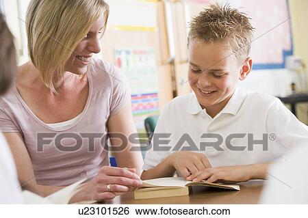 Stock Photograph - Student in class reading book with teacher. Fotosearch