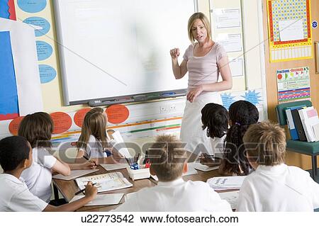 Stock Image - Students in class with teacher at board. Fotosearch