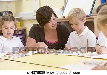 Stock Image - Students in class with teacher reading (selective focus). Fotosearch