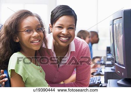 Picture - Teacher and student at computer terminal with students in background (selective focus/high key). Fotosearch