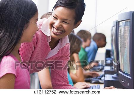 Teacher helping student at computer terminal with students in background (depth of field/high key) View Large Photo Image Stock Image - Teacher helping student at computer terminal with students in background (depth of field/high key). Fotosearch