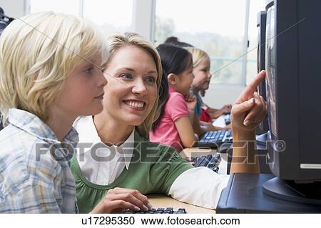 Teacher helping student at computer terminal with students in background (depth of field/high key) View Large Photo Image Stock Image - Teacher helping student at computer terminal with students in background (depth of field/high key). Fotosearch