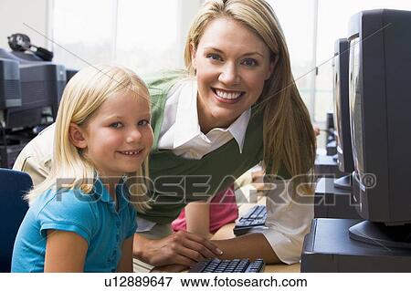 Teacher helping student at computer terminal with students in background (depth of field/high key) View Large Photo Image Stock Photo - Teacher helping student at computer terminal with students in background (depth of field/high key). Fotosearch