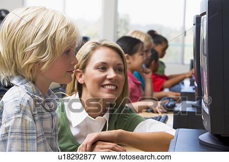 Teacher helping student at computer terminal with students in background (depth of field/high key) View Large Photo Image Stock Photo - Teacher helping student at computer terminal with students in background (depth of field/high key). Fotosearch