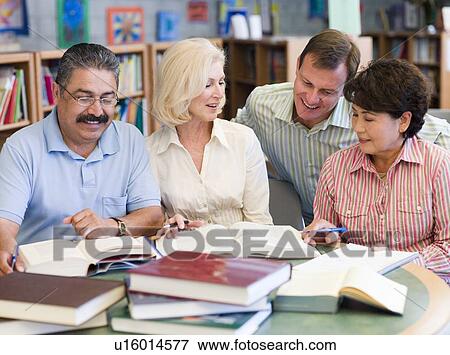 Three people sitting in library with books and notepads while a man leans over them (selective focus) View Large Photo Image Stock Photo - Three people sitting in library with books and notepads while a man leans over them (selective focus). Fotosearch
