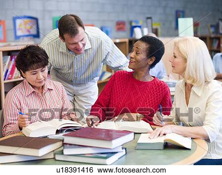 Stock Photograph - Three women sitting in library with books and notepads while a man leans over them (selective focus). Fotosearch