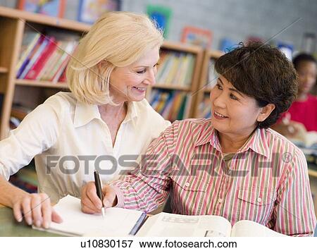 Stock Photo - Two women sitting in library with a book and notepad (selective focus). Fotosearch