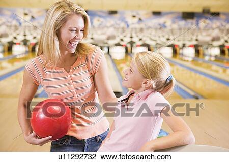 Stock Image - Woman and young girl in bowling alley holding ball and smiling. Fotosearch