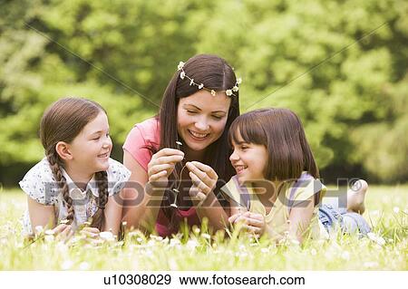 Mother and daughters lying outdoors with flowers smiling View Large Photo Image Stock Photo - Mother and daughters lying outdoors with flowers smiling. Fotosearch