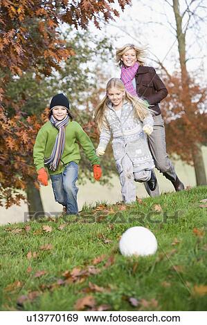 Stock Photo - Mother outdoors in park with two young children playing soccer and smiling (selective focus). Fotosearch