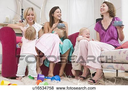 Stock Photo - Three mothers in living room with coffee and babies smiling. Fotosearch