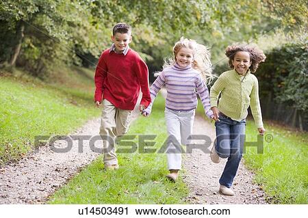 Stock Image - Three young friends running on a path outdoors smiling. Fotosearch