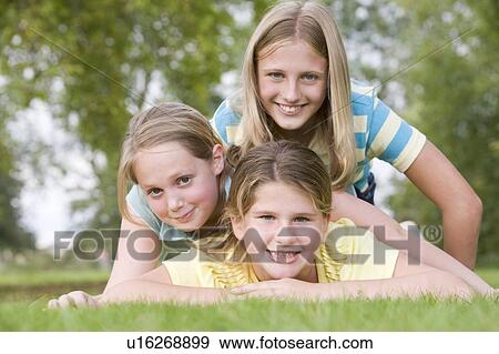 Stock Photo - Three young girl friends piled on each other outdoors smiling. Fotosearch