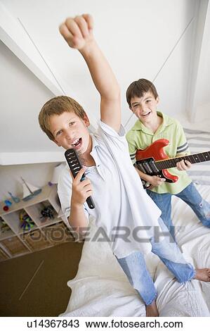 Stock Image - Two Boys Standing On A Bed, Playing Guitar And Singing Into A Hairbrush. Fotosearch