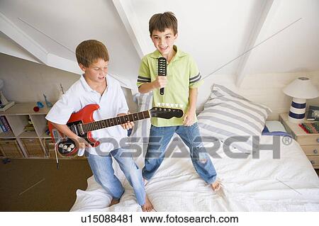 Stock Image - Two Boys Standing On A Bed, Playing Guitar And Singing Into A Hairbrush. Fotosearch