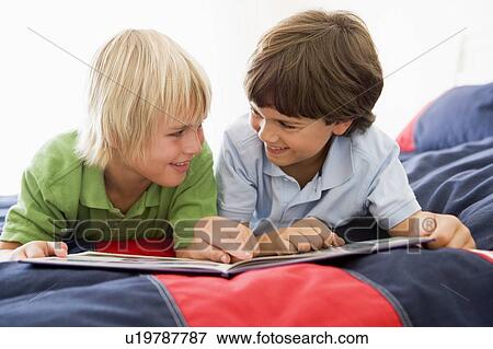 Stock Photo - Two Young Boys Lying Down On A Bed Reading A Book. Fotosearch