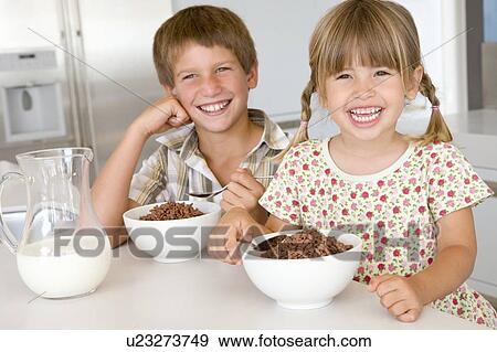 Stock Photo - Two young children in kitchen eating cereal smiling. Fotosearch