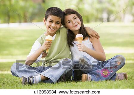 Two young children outdoors in park with ice cream smiling (selective focus) View Large Photo Image Picture - Two young children outdoors in park with ice cream smiling (selective focus). Fotosearch