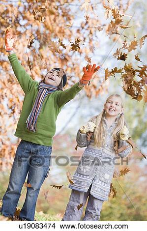 Two young children outdoors in park playing in leaves and smiling (selective focus) View Large Photo Image Picture - Two young children outdoors in park playing in leaves and smiling (selective focus). Fotosearch