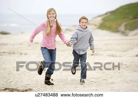 Stock Photo - Two young children running on beach holding hands smiling. Fotosearch