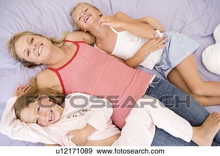 Woman and two young girls lying in bed playing and smiling View Large Photo Image Stock Photo - Woman and two young girls lying in bed playing and smiling. Fotosearch