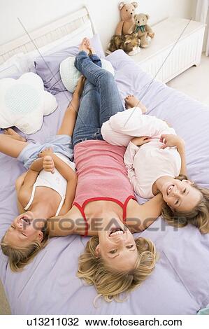 Woman lying in bed with two young girls laughing View Large Photo Image Stock Image - Woman lying in bed with two young girls laughing. Fotosearch