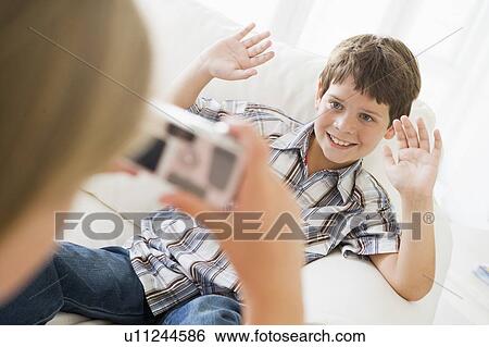 Stock Photograph - Young girl taking picture of smiling young boy with camera phone indoors. Fotosearch