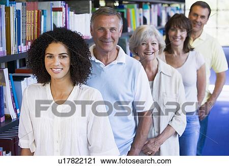 Stock Image - Five people in library standing by bookshelves (depth of field). Fotosearch