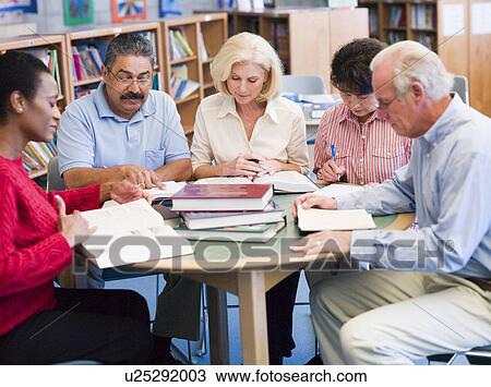 Stock Image - Five people sitting in library with books and notepads (selective focus). Fotosearch