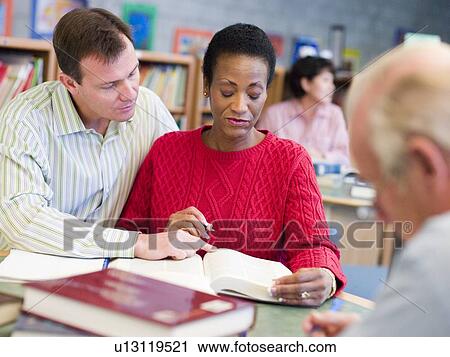 Stock Image - Man and woman sitting in library near man with a book and notepad (selective focus). Fotosearch