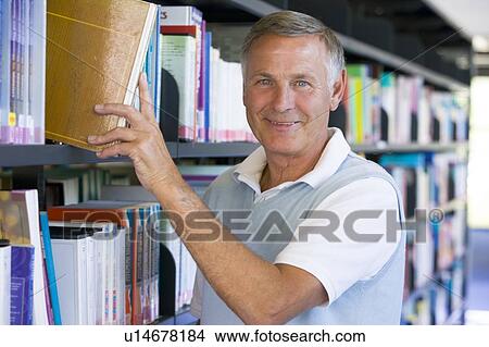 Picture - Man in library pulling book off a shelf (depth of field). Fotosearch