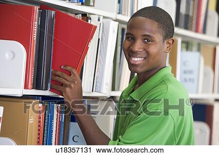 Stock Image - Man in library pulling book off a shelf (depth of field). Fotosearch