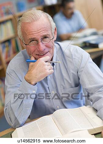 Stock Photography - Man in library with pen and book (selective focus). Fotosearch